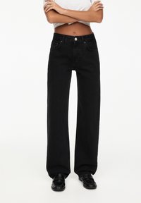 Zwarte wijde jeans gemaakt van denim, met een hoge taille, voorzakken en een knoopsluiting. Soepele textuur met minimale details.