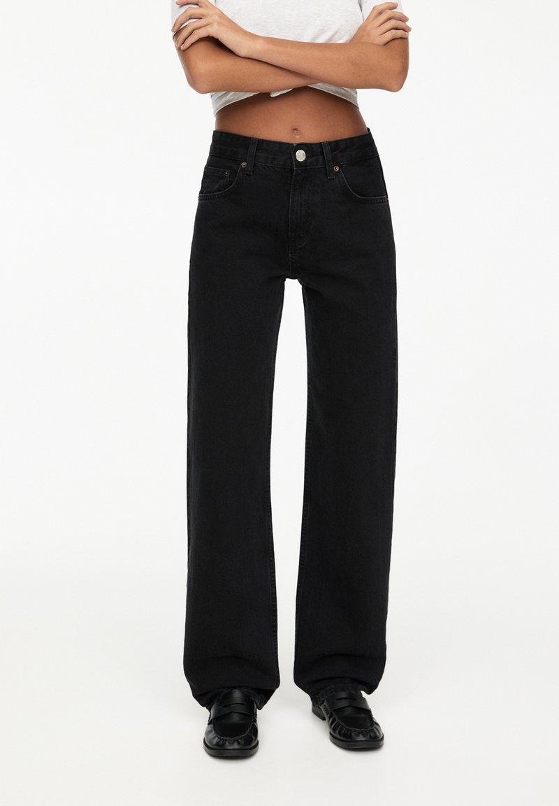 Zwarte wijde jeans gemaakt van denim, met een hoge taille, voorzakken en een knoopsluiting. Soepele textuur met minimale details.