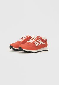 Zapatillas deportivas rojas con una parte superior de malla y tejido, que presentan cordones blancos y una marca. Suela de goma negra con un dibujo texturizado.