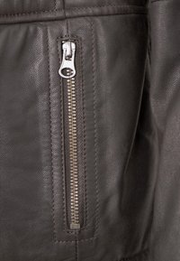 Dunkelgraue Lederjacke im Nahaufnahme mit einer seitlichen Reißverschlusstasche aus silbernem Metall und strukturierter Oberfläche. Detaillierte Nähte sichtbar.