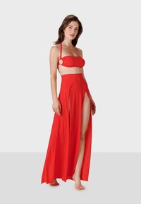 Conjunto de bikini rojo de dos piezas con un top tipo bandeau que presenta acentos de tirantes y una falda larga y dividida, hecha de una tela suave con una textura fluida.