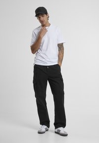 T-shirt en coton blanc, pantalon cargo noir avec poches latérales, et sneakers gris-blanc. Une casquette noire complète la tenue. Design simple, style décontracté.