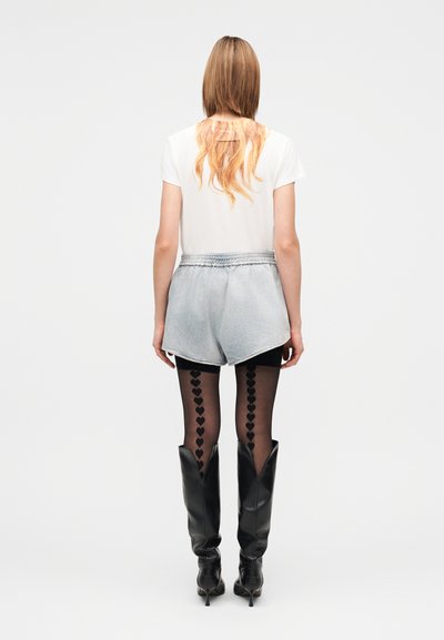 Biele tričko s grafikou vlasov na chrbte, doplnené svetlomodrými rifľovými šortkami, čiernymi pančuchami s motívom srdiečok a čiernymi čižmami po kolená.