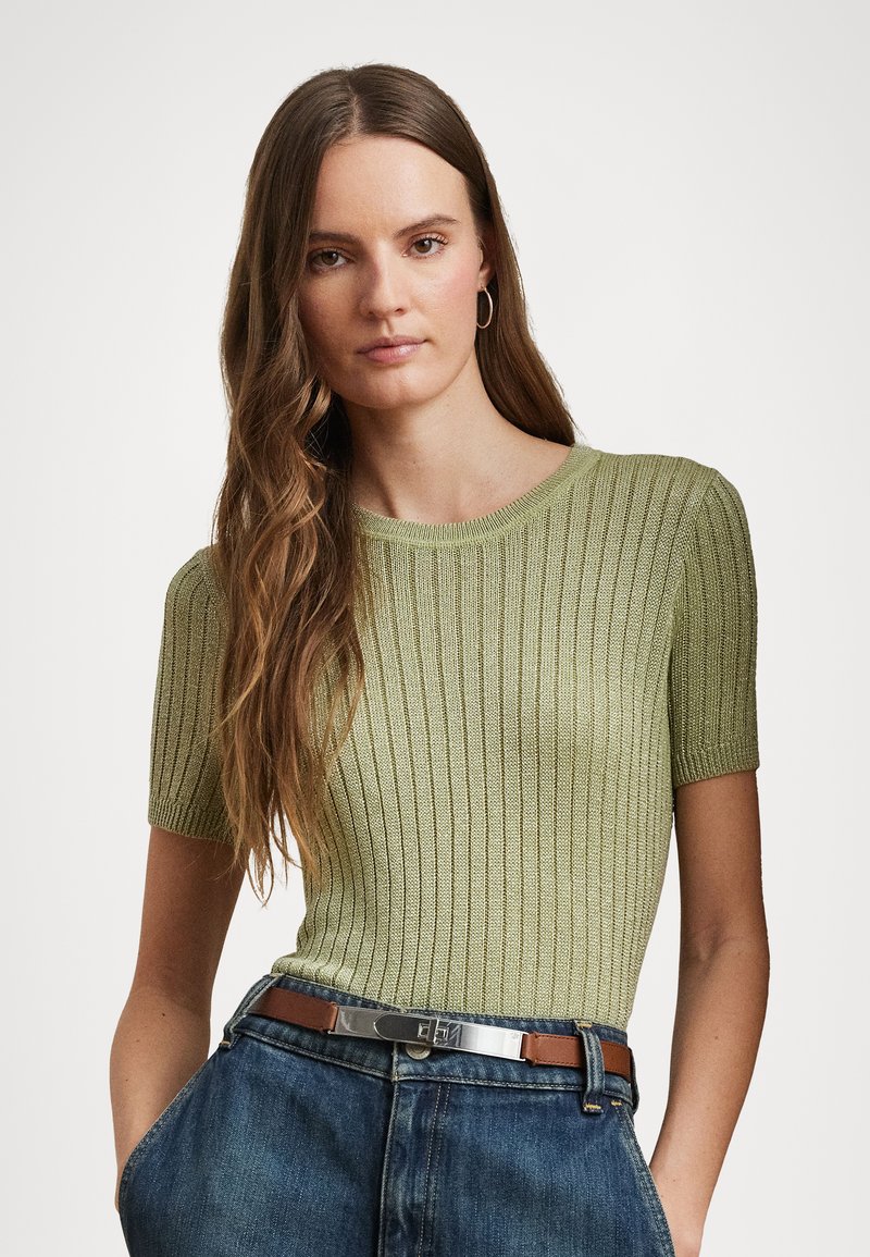 Short-sleeve ribbed top in light green, featuring a round neckline and textured knit. Paired with high-waisted denim jeans and a brown belt.