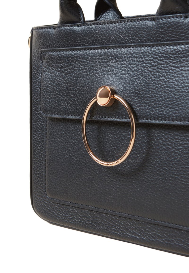 Sac à main en cuir noir avec une finition texturée, une poche avant et un accent matériel circulaire doré bien en vue.