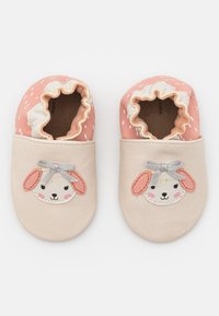 Pehmeästä nahasta valmistetut vauvan tossut persikka- ja kermansävyssä. Varustettu pupunkasvojen designilla, jossa on kirjottu korvat, hopeinen rusetti ja röyhelöavaus.