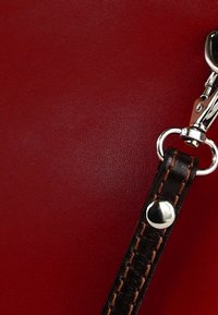 Rood lederen materiaal met een gladde textuur, voorzien van een zilveren metalen clip en een bruine riem met contrasterende stiksels en een metalen gespaccent.