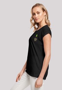 Čierne tričko s rolovanými rukávmi, na ktorom je zelená grafika uhorky a text "Pickle Rick" na hrudi. Biele nohavice dopĺňajú outfity.