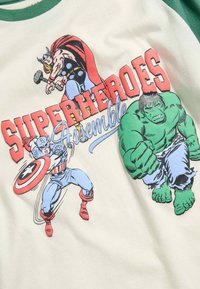 Krémové tričko s zelenými raglánovými rukávy s motivem superhrdinů v komiksovém stylu: Thor, Captain America a Hulk. Text zní "SUPERHEROES Assemble."