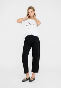 Vit t-shirt med färgglada pärldekorationer, matchad med högmidjade svarta jeans med nitar och rak skärning.