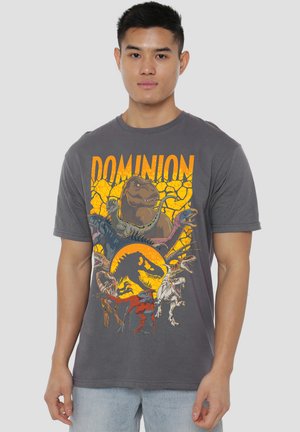 Young man wearing a gray t-shirt with the word "DOMINION" and colorful dinosaur illustrations on the front.