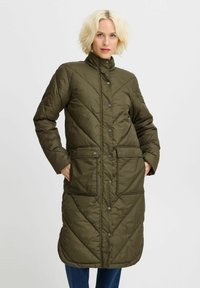 Manteau long matelassé vert olive avec col montant, boutons-pression et deux poches avant. Texture lisse avec un motif chevron.