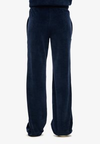 Granatowe spodnie z weluru o luźnym kroju, z bocznymi kieszeniami i gładką, miękką strukturą. Elastyczny pas dla większego komfortu.