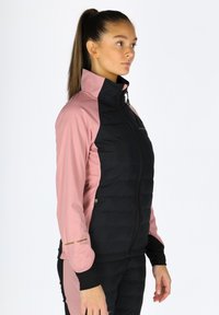 Gepolsterte schwarze und pinke Jacke mit hohem Kragen, langen Ärmeln und Reißverschluss. Sie hat eine Mischung aus glatten und gesteppten Texturen. Goldene Akzente an den Ärmeln.