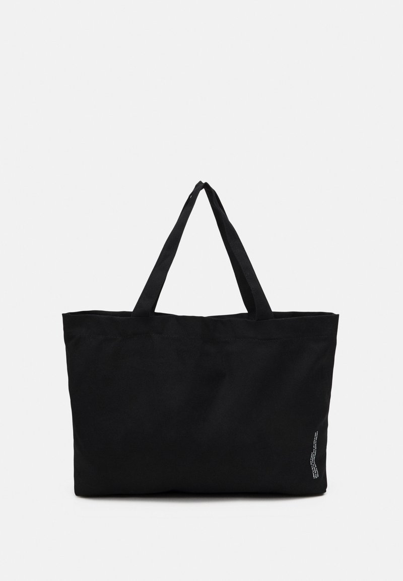 Svart tote-väska i kraftig tyg, med två långa handtag och en enkel rektangulär form. Inga mönster eller ytterligare detaljer synliga.
