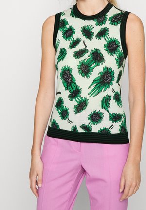 Top blanco sin mangas con ribete negro y estampado floral verde combinado con pantalones rosas de cintura alta usados por una persona.