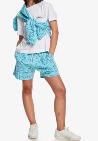 Ljust turkosa shorts med abstrakta lila mönster, ihopkopplade med en vit t-shirt och en matchande knuten jacka. Har dragsko i midjan.