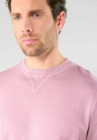 Felpa rosa chiaro con collo tondo e dettagli a costine, che mostra una texture liscia e morbida e un minimo di dettagli di cucitura.