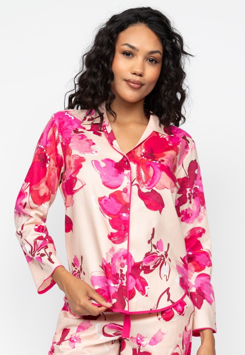 Bloemig pyjamastel dat een lichtroze basis heeft, grote roze en rode bloempatronen, een geknipt kraagje, knopen aan de voorkant en contrasterende afwerking.
