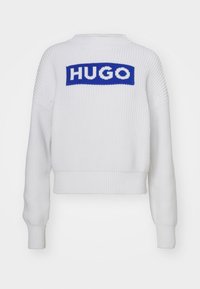 Maglione bianco lavorato a maglia con una toppa rettangolare blu con la scritta "HUGO". Il design include polsini a coste e un collo rotondo.