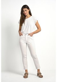 Haut blanc à manches courtes associé à un jean ajusté de couleur claire. Des sandales à lanières tressées remarquables complètent la tenue. Design simple et épuré.