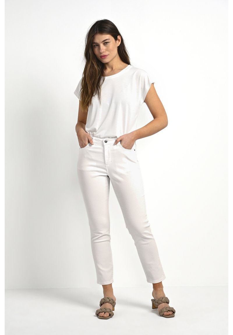 Haut blanc à manches courtes associé à un jean ajusté de couleur claire. Des sandales à lanières tressées remarquables complètent la tenue. Design simple et épuré.