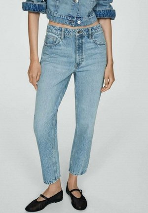 Woman wearing light blue high-waist straight jeans, cropped denim jacket, and black Mary Jane flats, standing against a plain background.