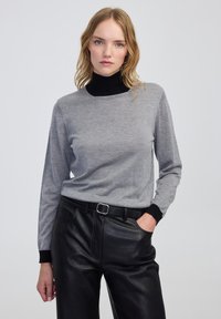 Haut gris à manches longues avec un col roulé noir, fabriqué dans un matériau doux. Associé à un pantalon en cuir noir avec une taille ceinturée.