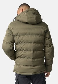 Olivengrøn pufferjakke med aftagelig hætte, kviltet tekstur og sorte snore. Har horisontale syninger og en lige kant.