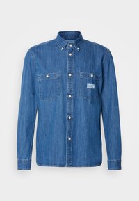 Blue denim shirt featuring a button-down collar, two chest pockets, and white snap buttons. Smooth texture with visible stitching details.