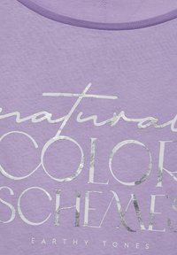 Lila kangas, jossa on hopeametalliväriä oleva teksti, joka lukee "luonnolliset VÄRIPALLOMIT MAAPERÄISET SÄVYT" sekoitetuilla fonteilla.