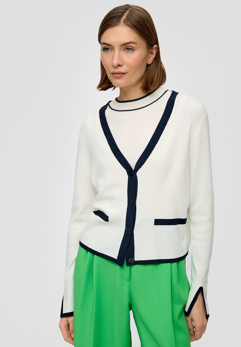 Witte cardigan met marineblauwe rand, met een V-hals, vijf knopen en zijzakken. Mouwen met marineblauwe accenten. Felgroene broek.
