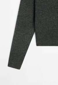 Manche de pull en tricot gris foncé avec poignets et ourlet côtelés sur fond blanc, montrant la texture et les détails du tissu.
