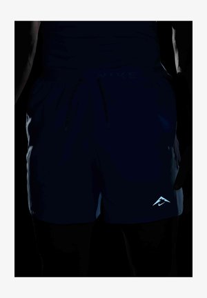 Nike hlače v temno modri barvi, ki imajo elastični pas z vrvico in odsevnimi podrobnostmi logotipa na spodnjem levem robu. Gladka tekstura.