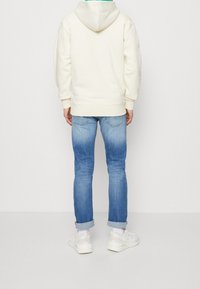 Sweat à capuche crème avec capuche, associé à un jean bleu clair fuselé et des baskets blanches. Le tissu semble doux ; le jean présente un effet délavé.