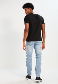 T-shirt preta de gola redonda, design justo, combinada com jeans azul claro com bolsos traseiros e um leve desgaste. Ténis pretos completam o visual.