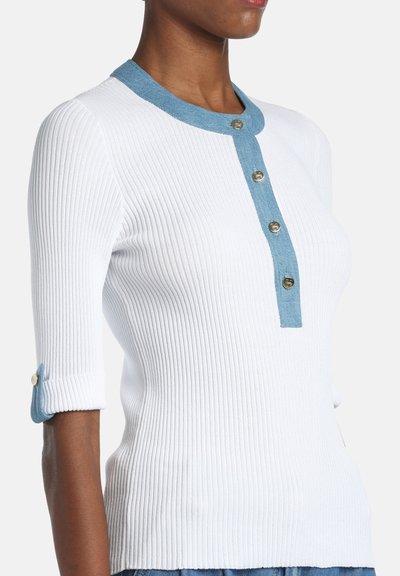 Pull blanc côtelé avec un col bleu clair et une patte de boutonnage assortie, manches retroussées soulignées par la même teinte de bleu.