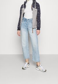 Grå och marinblå zip-up hoodie med stjärnmönster, vit polokrage, ljusblå vida jeans och vita/grå sneakers med gula detaljer.