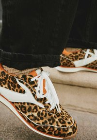Leopardenmuster-Sneaker mit weißen Akzenten, orangen Details und weißen Schnürsenkeln. Hergestellt aus strukturiertem Stoff mit klassischem sportlichem Silhouetten.