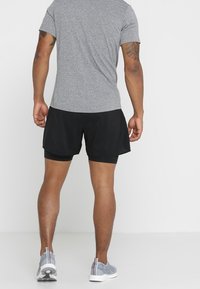 Šedé sportovní tričko a černé šortky, které mají volný střih a hladkou texturu. Obuv tvoří šedé tenisky s vzorovaným designem.