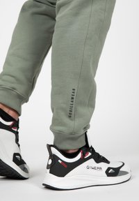 Lichtgroene joggers met een geribbelde manchette en zijbranding, gecombineerd met wit-zwart sport schoenen met rode accenten en textuur. 