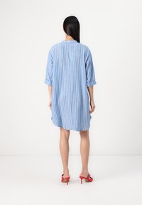 Vestido camisa oversized de riscas azuis e brancas, com mangas três quartos, textura suave e fendas laterais, visto de costas.