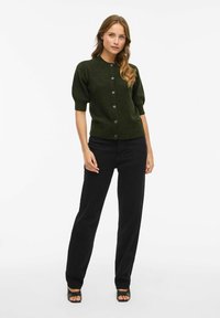 Cardigan vert foncé avec des manches courtes bouffantes, fermeture à boutons à l'avant et ourlet côtelé ; associé à un pantalon noir et des talons ouverts noirs.