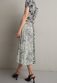 Czarna i biała sukienka w wzory z krótkimi rękawami, o długości midi, z kontrastującym kwiatowym wzorem z jednej strony. Noszona z czarnymi sandałami na obcasie.