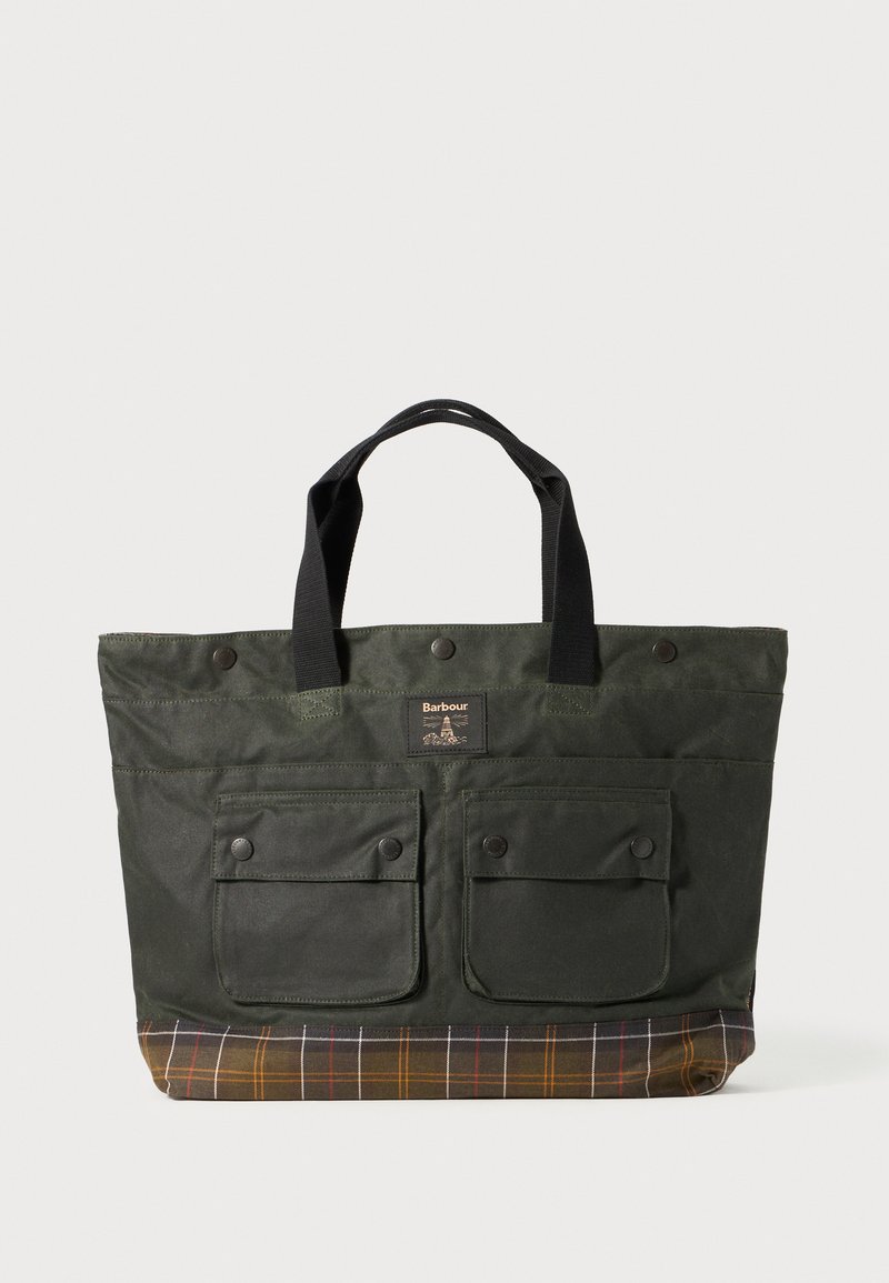 Saco de lona verde com dois bolsos frontais com botão de pressão, alças pretas e um fundo com padrão xadrez em tons de castanho, amarelo e roxo.