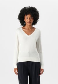 Pulover z V-izrezom in dolgimi rokavi v off-white barvi, izdelan iz mehkega pletenega materiala z rebrastimi detajli na robu in manšetah.