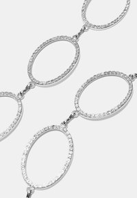 Stříbrný řetízek se spojenými oválnými tvary. Každý ovál je zdobený průhlednými rhinestone kamínky podél okraje, což vytváří třpytivý efekt.