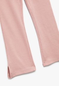 Leggings côtelés rose pâle avec des poignets évasés, présentant une texture douce et des coutures bien finies, conçus pour le confort et la facilité de mouvement.