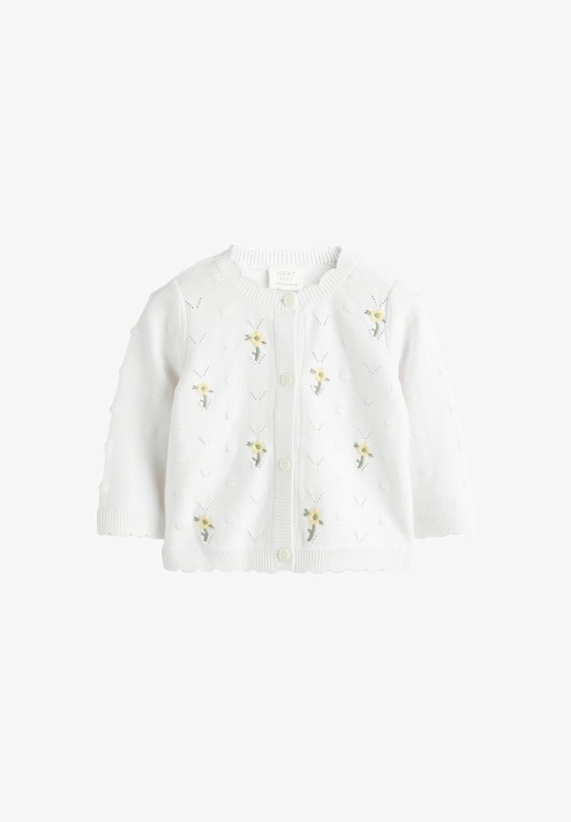 Cardigan bianco lavorato a maglia per neonati con piccole ricami floreali gialli e un motivo testurizzato. Ha un collo rotondo e chiusura a bottoni.