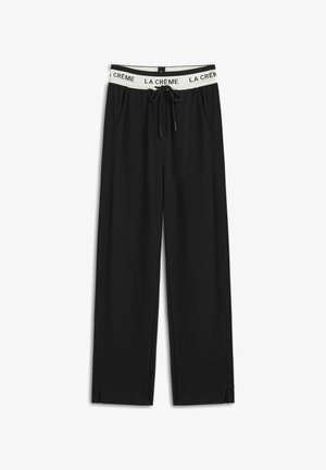 Pantalones de pierna ancha negros, hechos de tela suave, con una cinturilla elástica blanca que lleva el texto "LA CRÈME" y bolsillos laterales.